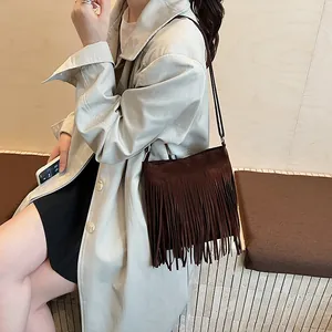 Sac seau bandoulière en daim marron foncé avec franges bohèmes porté sur un trench beige