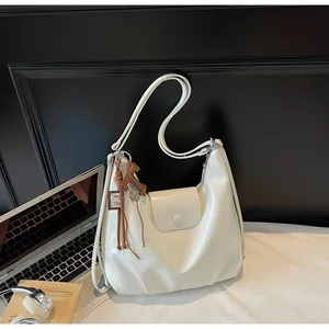 Gros plan du sac hobo blanc à finition brillante et breloque décorative à pompon marron