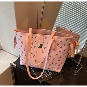 Close-up of pink cherry print tote bag with a golden metal logo plate and long straps