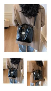Detail of a black glossy handbag with a triangular logo and adjustable strap