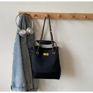 Detail of black quilted tote bag with gold swivel lock and chain strap on wooden hook
