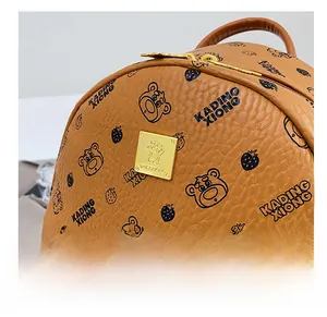 Détail d'un sac à dos en similicuir marron avec ours imprimés et plaque logo dorée