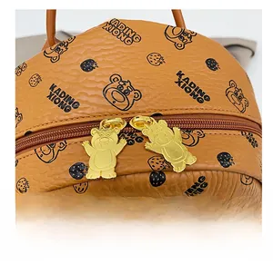 Détail des fermetures éclair dorées en forme d'ours sur un sac à dos en cuir marron