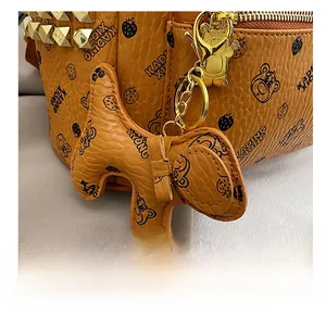 Gros plan sur la texture cuir marron avec rivets dorés et breloque chien sur le sac à dos