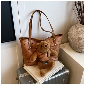 Borsa tote marrone con orsetto di peluche 3D e motivi grafici appoggiata su una valigia