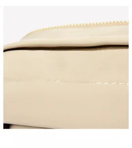 Detailed macro view of beige nylon fabric with white stitching and gold metal zipper