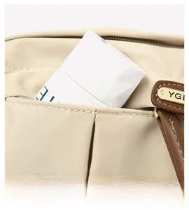 Close-up of beige nylon bag detail featuring brown leather trim and golden metal logo plate
