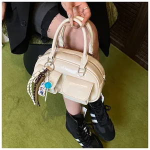 Detail of cream glossy pillow bag featuring front pockets and cute bear charm accessories