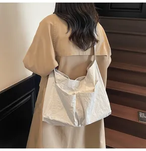 Detail of a white oversized tote bag with pleated nylon fabric shown on model's shoulder