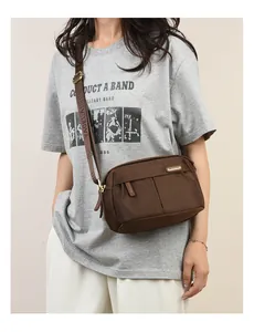 Detail of adjustable wide shoulder strap with metal buckle on brown oxford crossbody bag