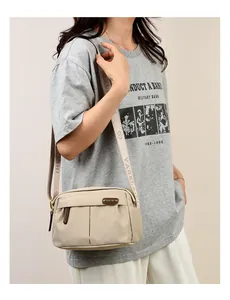Close-up of beige waterproof nylon crossbody bag featuring wide branded woven shoulder strap