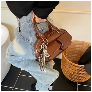 Detail of a dark brown glossy PU leather Boston bag featuring dual front pockets and charm