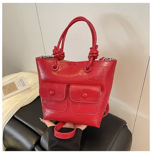 Detail of red crocodile embossed handbag featuring front flap pockets and knotted handle