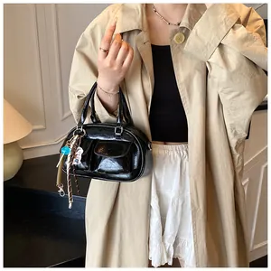 Detail of glossy black bowling bag with front pockets and trendy charms on beige trench coat