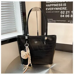 Détail d'un sac cabas noir à texture crocodile avec logo argenté et charm ours peluche