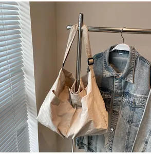 Detail of a beige tote bag showing the side pocket with an adjustable plastic buckle strap