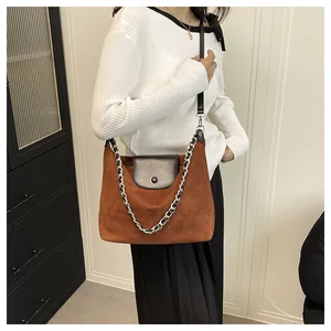 Close-up of retro brown suede tote bag with black leather flap and metal chain strap