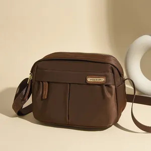 Deep brown oxford cloth crossbody bag with satin finish and golden metallic zipper detail