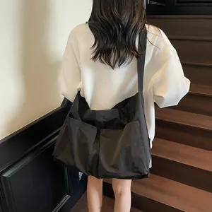Large black nylon tote bag shown on person's back with spacious outer pockets and wide strap