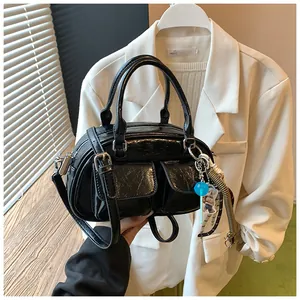 Detail of black glossy leather satchel with dual front pockets and decorative charms