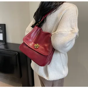 Detail of dark red faux leather bag with elegant gold flower lock on white sweater