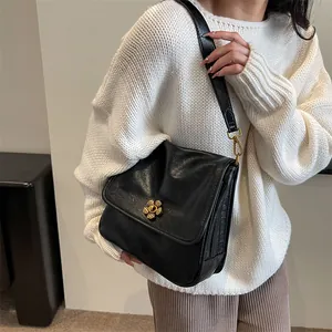 Chic black crossbody bag with gold floral clasp shown on a model with a knit sweater
