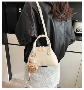 Model view of a cream leather shell bag with a teddy bear charm and crossbody strap