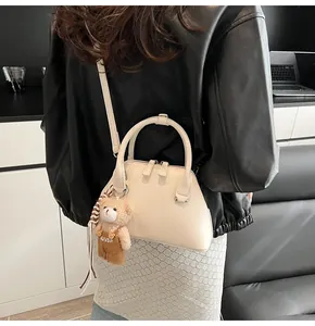 Rear view of model wearing off-white shell handbag with a cute teddy bear pendant charm