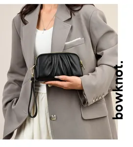 Detail of black pleated leather clutch with lychee texture and gold zipper worn by model