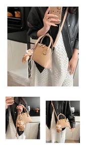 Detail of tan leather crossbody shell bag featuring a cute plush bear pendant accessory