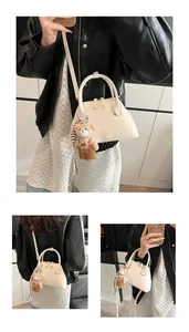 Detail of a creamy white shell-shaped handbag with dual handles and a cute bear charm