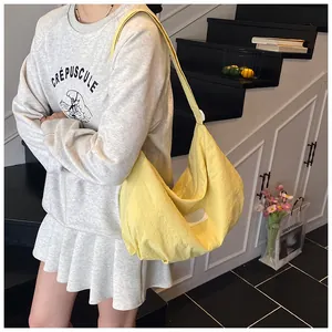 Detail of a large pale yellow nylon hobo tote bag worn as a shoulder bag on a model