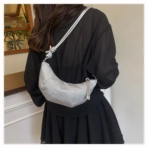 Nahaufnahme einer silbernen Croissant-Tasche mit Knotengurt und Quastenanhänger