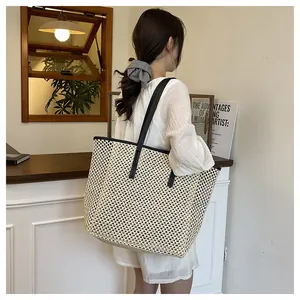 Close-up of a large beige straw woven tote bag with black contrast straps and buckles