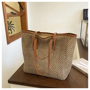 Detailed view of straw tote bag with brown faux leather straps on a wooden table