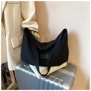 Detail of the TZIMEI logo patch on a large black canvas crossbody bag on a silver suitcase