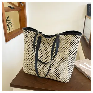 Detail of hollow-out woven straw tote bag with black leather straps and mesh texture