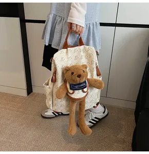 Detailed view of cream backpack with bear prints and a 3D plush doll accessory