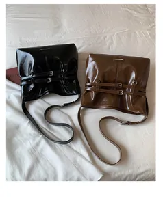 Nahaufnahme schwarzer und brauner glänzender Ledertaschen mit Schnallen auf weißem Bett