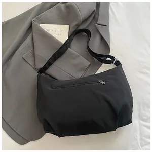 Detailed close-up of a black crescent nylon crossbody bag on a grey suit jacket background