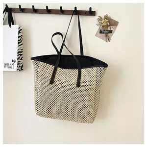 Detail of a woven straw tote bag with black leather straps hanging on a wall hook