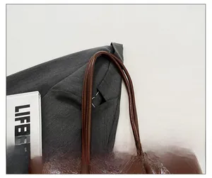 Detail of dark brown leather tote bag showing grainy texture and stitching on the straps