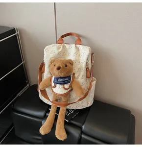Detail of a beige backpack featuring teddy bear patterns and a plush bear doll attachment