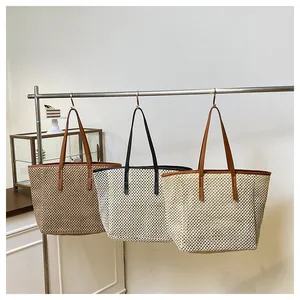Three large straw woven tote bags with leather handles hanging in a minimalist showroom