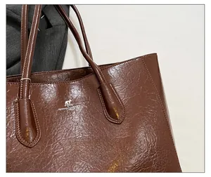 Detail of dark brown tote bag showing oily wax leather texture and logo stitching