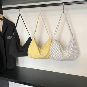 Three minimalist canvas hobo bags in black, yellow, and plaid shown in a closet scene