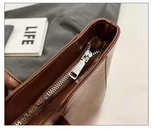 Close-up of smooth metal zipper and premium leather texture on brown tote bag
