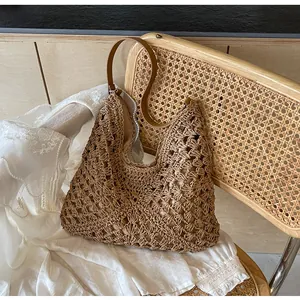 Gros plan d'un grand sac cabas en paille ajouré avec bandoulière en cuir brun sur chaise