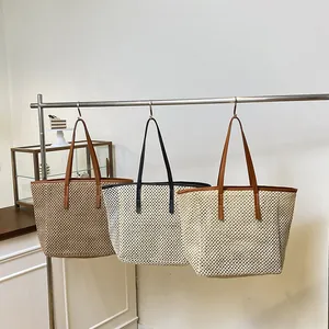 Three assorted woven straw tote bags with faux leather straps hanging in a minimalist studio