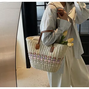 Detail of woven straw tote bag with pink diamond pattern and brown leather handles